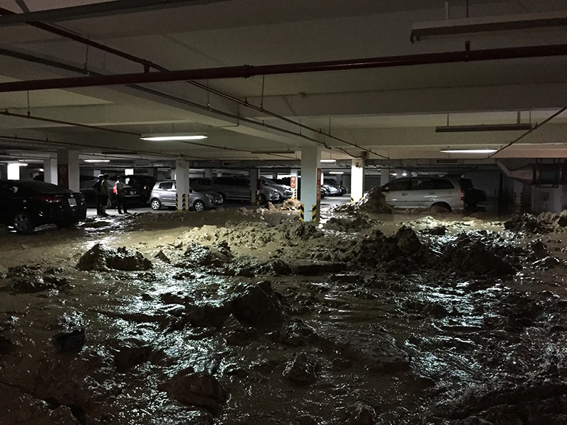 Bức tường bị vỡ khiến hàng trăm tấn bùn đất tràn vào nhà để xe của chung cư vùi ô tô và xe máy.